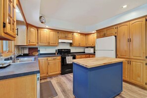 A kitchen with wooden cabinets, a black stove, a white refrigerator, and a blue island. - Dog Friendly Home in Sturgeon Bay with fire pit (Sturgeon Bay)