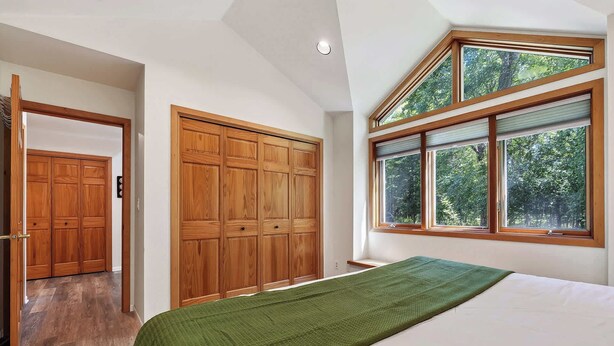 Un dormitorio con una cama grande, un armario de madera y una ventana con vistas a árboles.