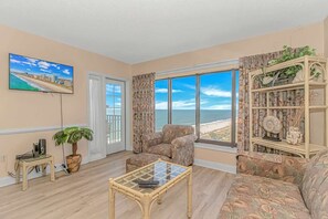 A living room with a large window, a sofa, a chair, a coffee table, a TV, and a bookshelf with decorative items. - Palace 809 Ocean View Escape (Myrtle Beach)