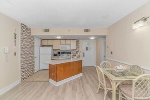 A compact kitchen with a central island, a dining table with chairs, and a microwave above the island. - Palace 809 Ocean View Escape (Myrtle Beach)