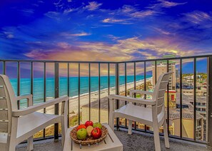 A balcony with two chairs, a wicker basket with apples, and a view of the beach and ocean. - Palace 809 Ocean View Escape (Myrtle Beach)
