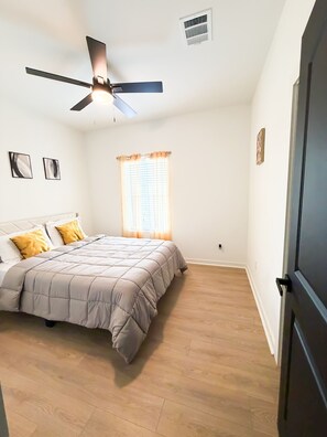 Un dormitori amb llit, ventilador de sostre, finestra amb cortines i una porta.