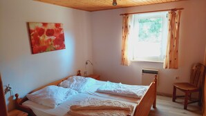 Ein Schlafzimmer mit einem Holzbett, einem Nachttisch, einem Sessel, einem Fenster mit Vorhängen und einem Bild an der Wand.