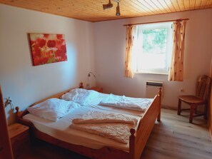Ein Schlafzimmer mit einem Holzbett, einem Nachttisch, einem Sessel, einem Fenster mit Vorhängen und einem Bild an der Wand.