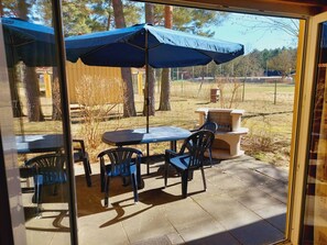 Eine Terrassengruppe im Freien mit Tisch, Stühlen, einem blauen Sonnenschirm und einer Feuerstelle.