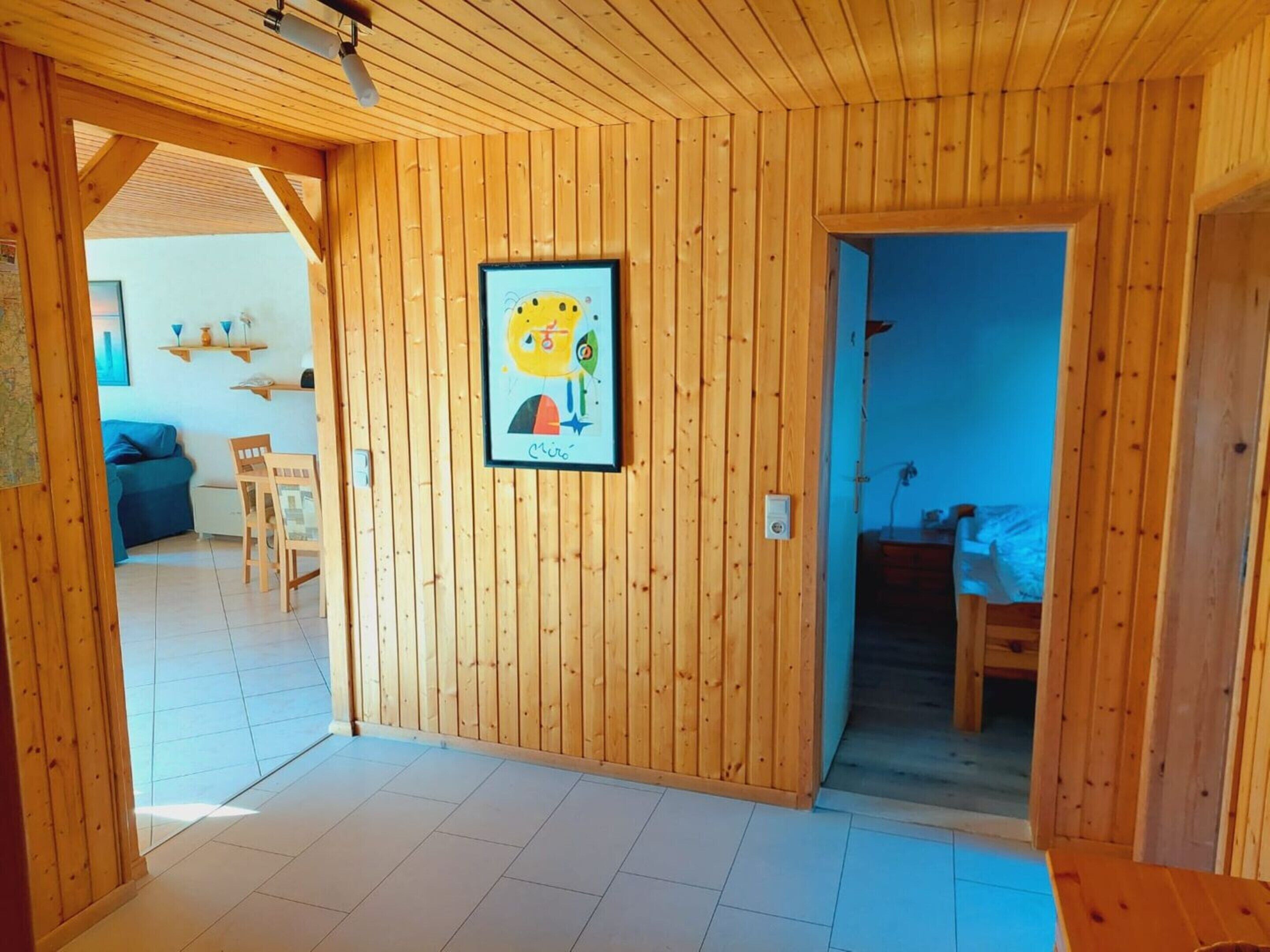 Un interno in legno con un quadro appeso al muro, una zona pranzo con sedie e una cucina visibile.