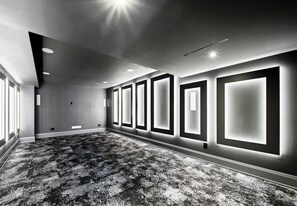 A hotel room with a large carpeted area, recessed ceiling lights, and a wall with illuminated panels.