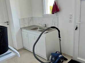 A compact kitchen with a sink, a window, and a vacuum cleaner.