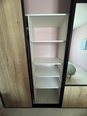 Avoimet ovet paljastavat vaatekaapin, jonka hyllyt ovat tyhjät ja jossa on puinen ovenkarmi.