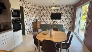 A modern kitchen with a dining area, a flat-screen TV, and a large window. - Les Parures d’Anthésim 20 : Cotentin – A/C & Green'Up EV Charger (Saint-Floxel)