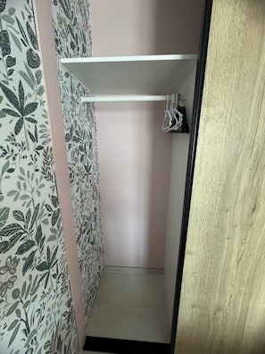 Ein kleiner, schmaler Raum mit einer rosafarbenen Wand, einem weißen Regal und einer Holztür.