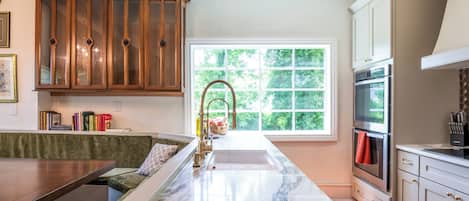 A kitchen with a marble countertop, wooden cabinets, a built-in bench, and a window with a view of greenery.
