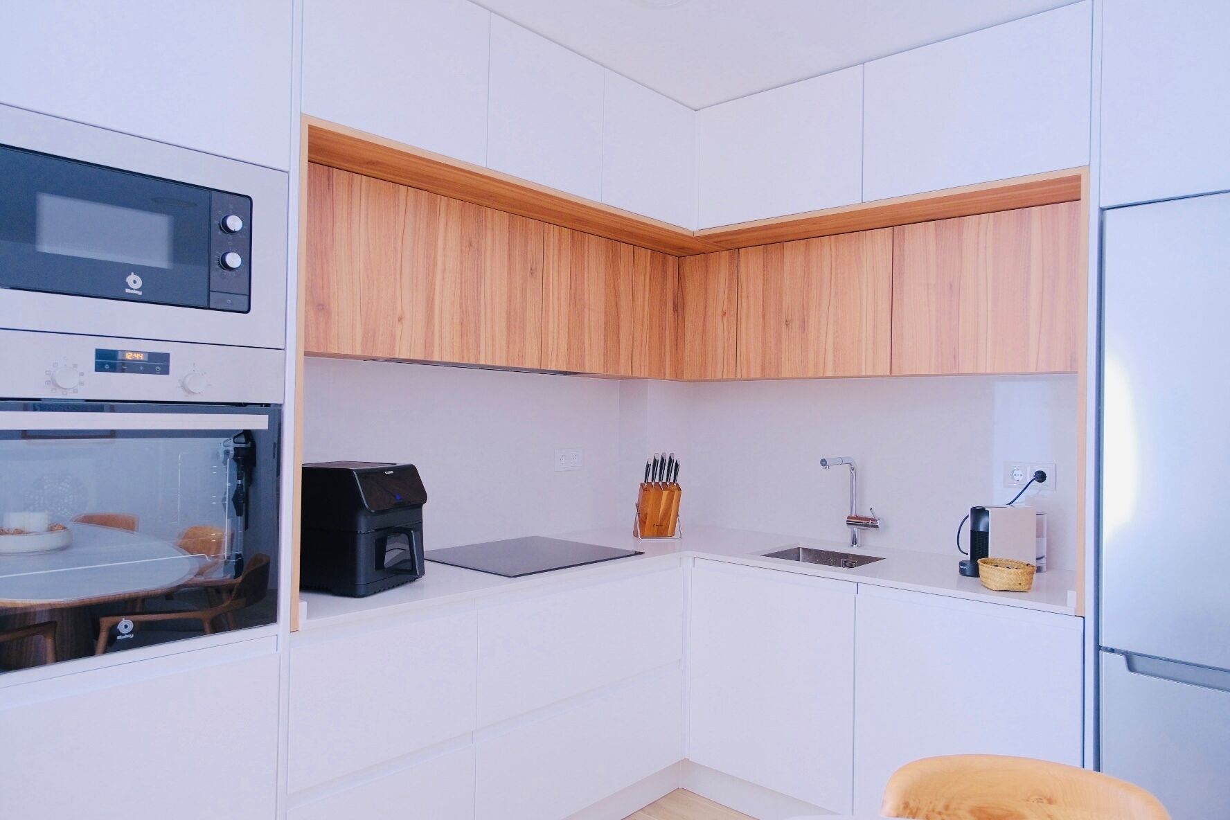A compact kitchen with a microwave, coffee machine, sink, and wooden cabinets.