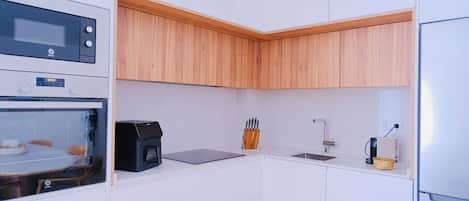 A compact kitchen with a microwave, coffee machine, sink, and wooden cabinets.