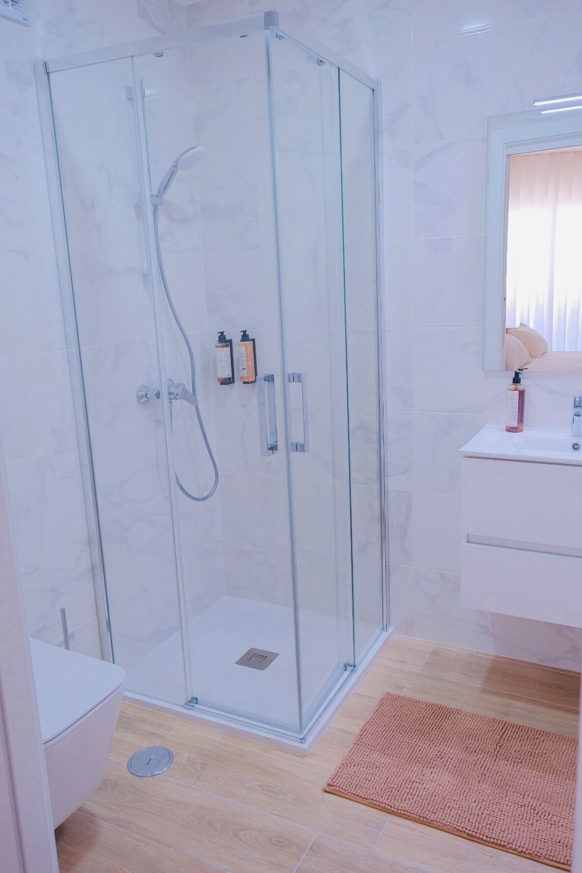 Un baño moderno con ducha de vidrio, lavamanos con artículos de aseo y un espejo.