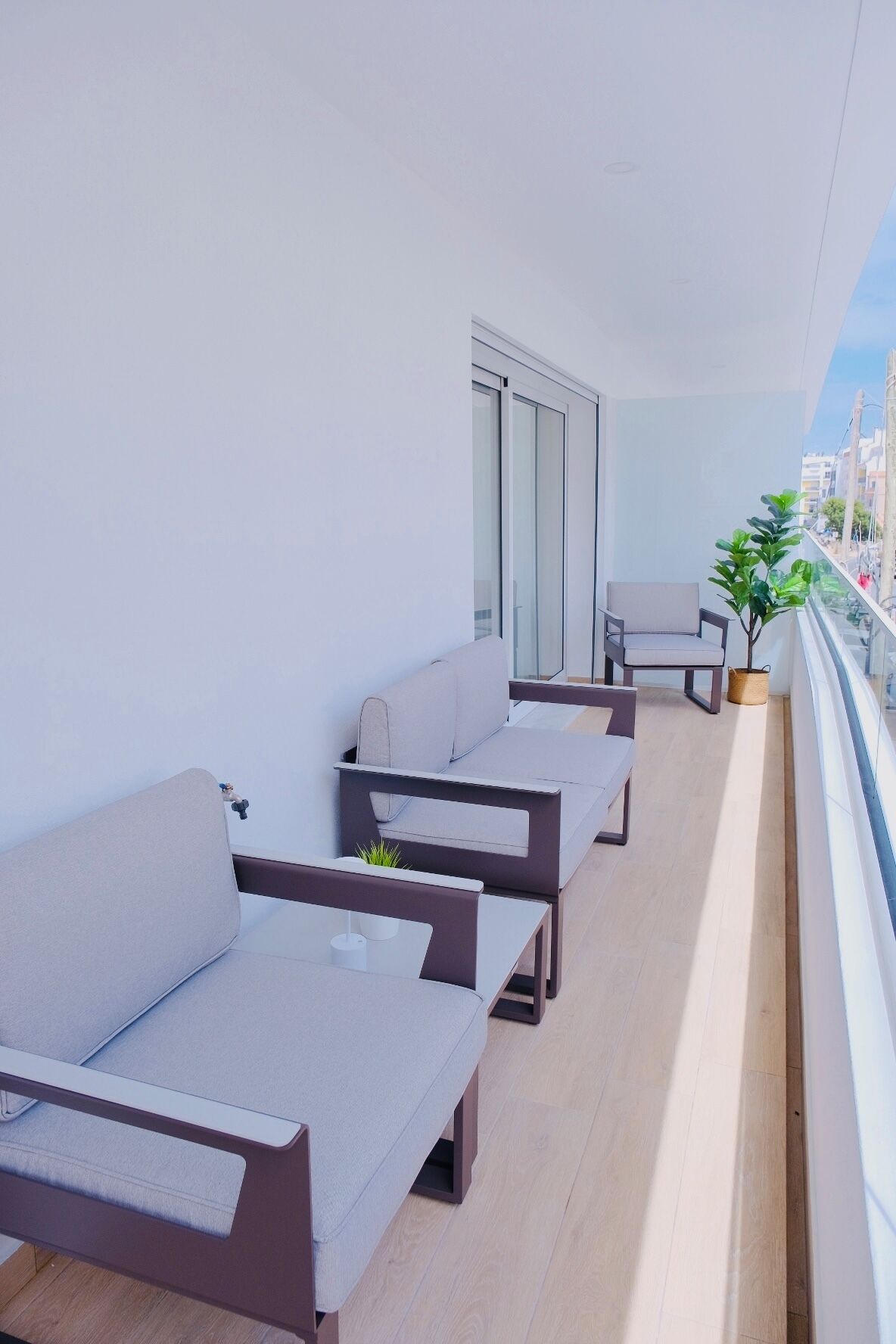 Un balcon avec trois canapés et une petite table, une plante en pot et une vue sur la ville.