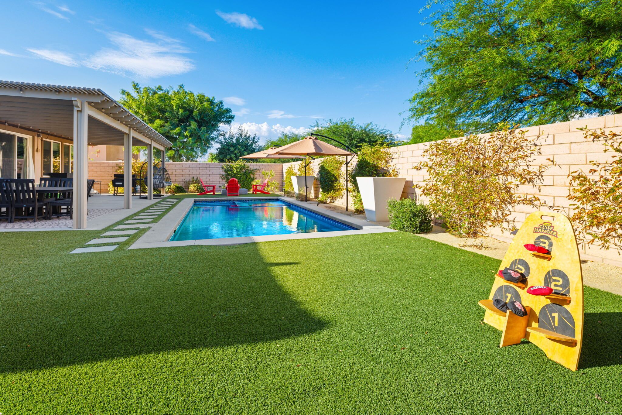 A backyard with a swimming pool, a covered patio, and a bocce court.