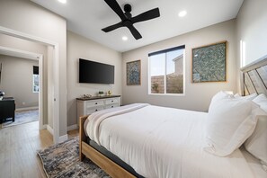 Une chambre à coucher avec un lit, un ventilateur de plafond, des œuvres d’art et un téléviseur.