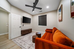 Un salon moderne doté d’un ventilateur de plafond, d’un téléviseur à écran plat, d’une fenêtre avec des stores, d’un canapé, d’une table basse et d’un tapis.