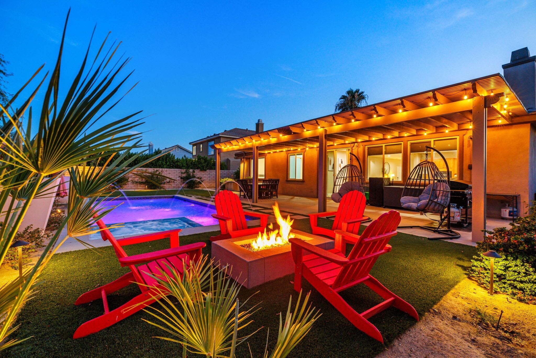 Un jardin avec un jacuzzi, un espace salon extérieur et une pergola illuminée de guirlandes lumineuses.