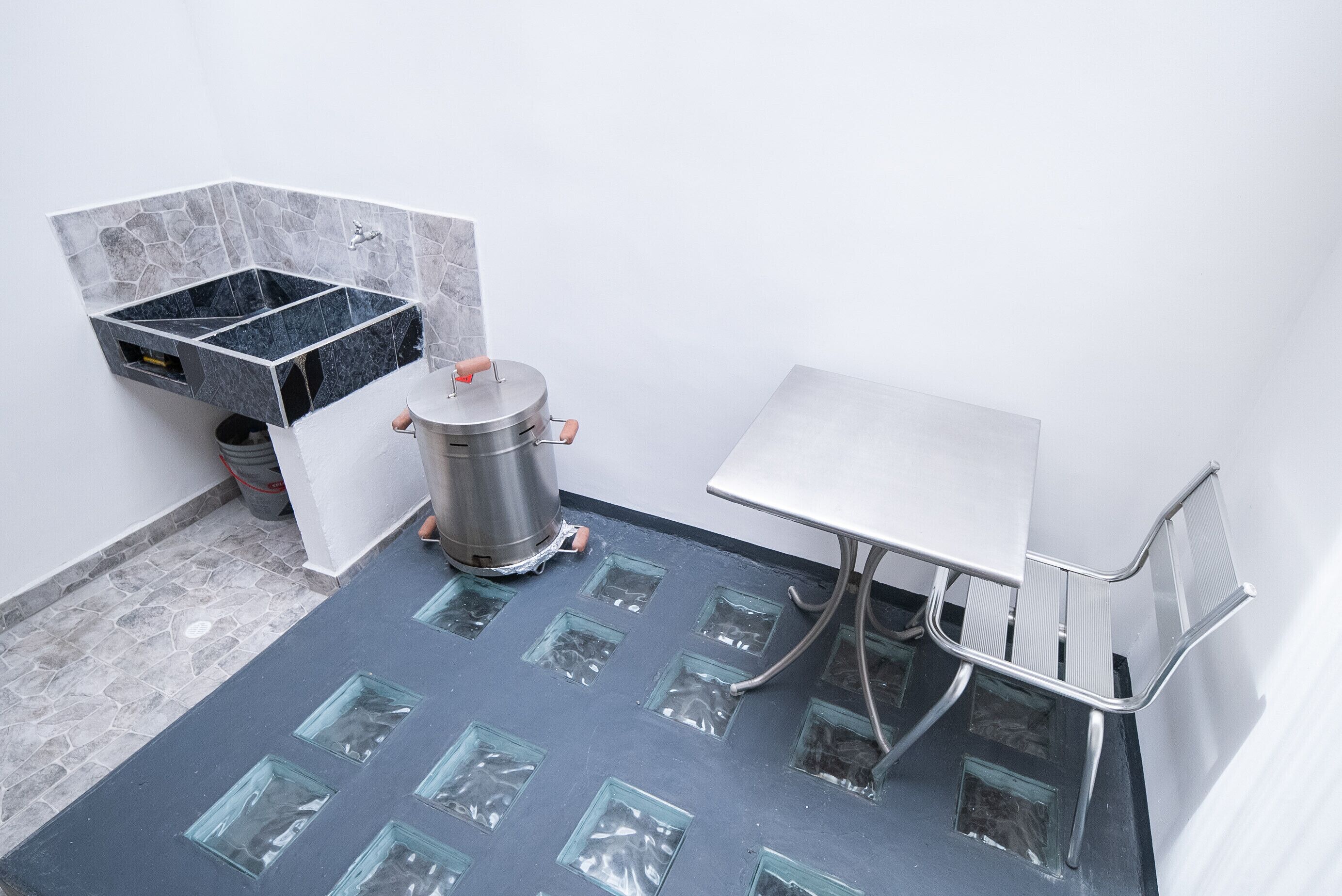 A bathroom with a tiled floor, a sink, a trash bin, and a shower area.