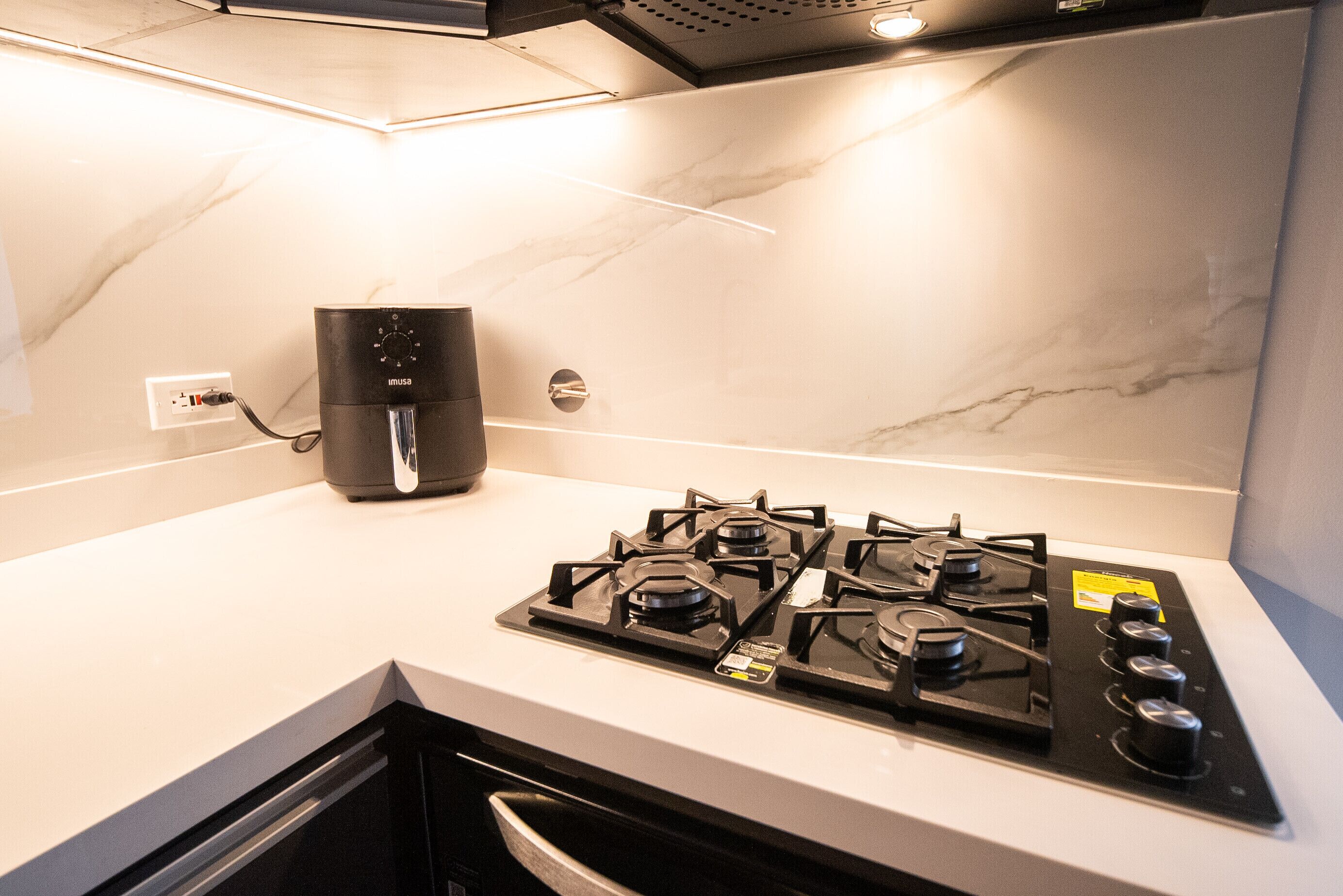A kitchen with a gas stove, a coffee maker, and a marble backsplash.