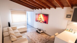 Ein Wohnzimmer mit einer Couch, einem flachbildfernseher an der Wand, einem Kamin und einem Fenster mit Jalousien.