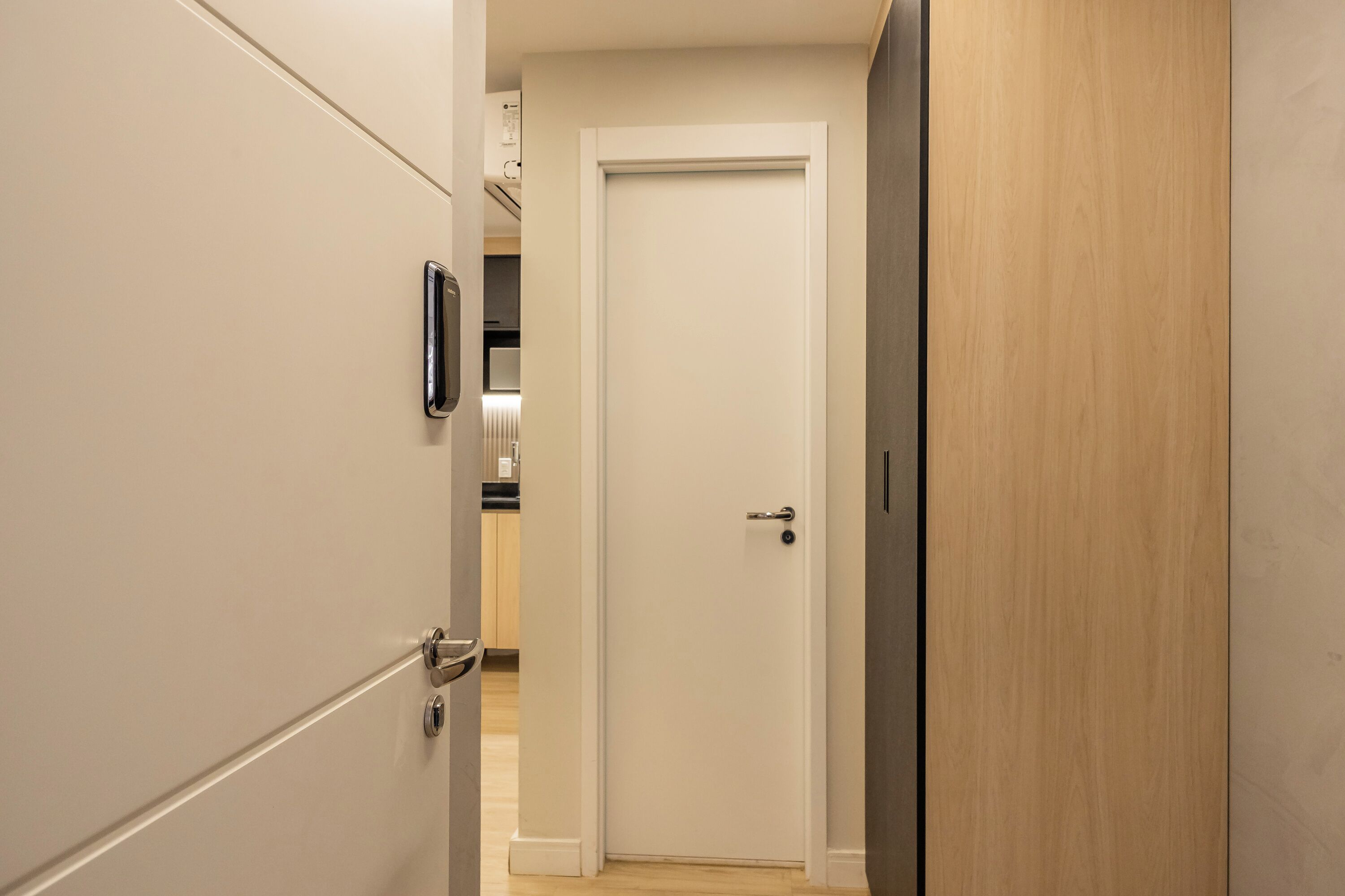 Un pasillo con una puerta blanca, una puerta de madera y un picaporte metálico.