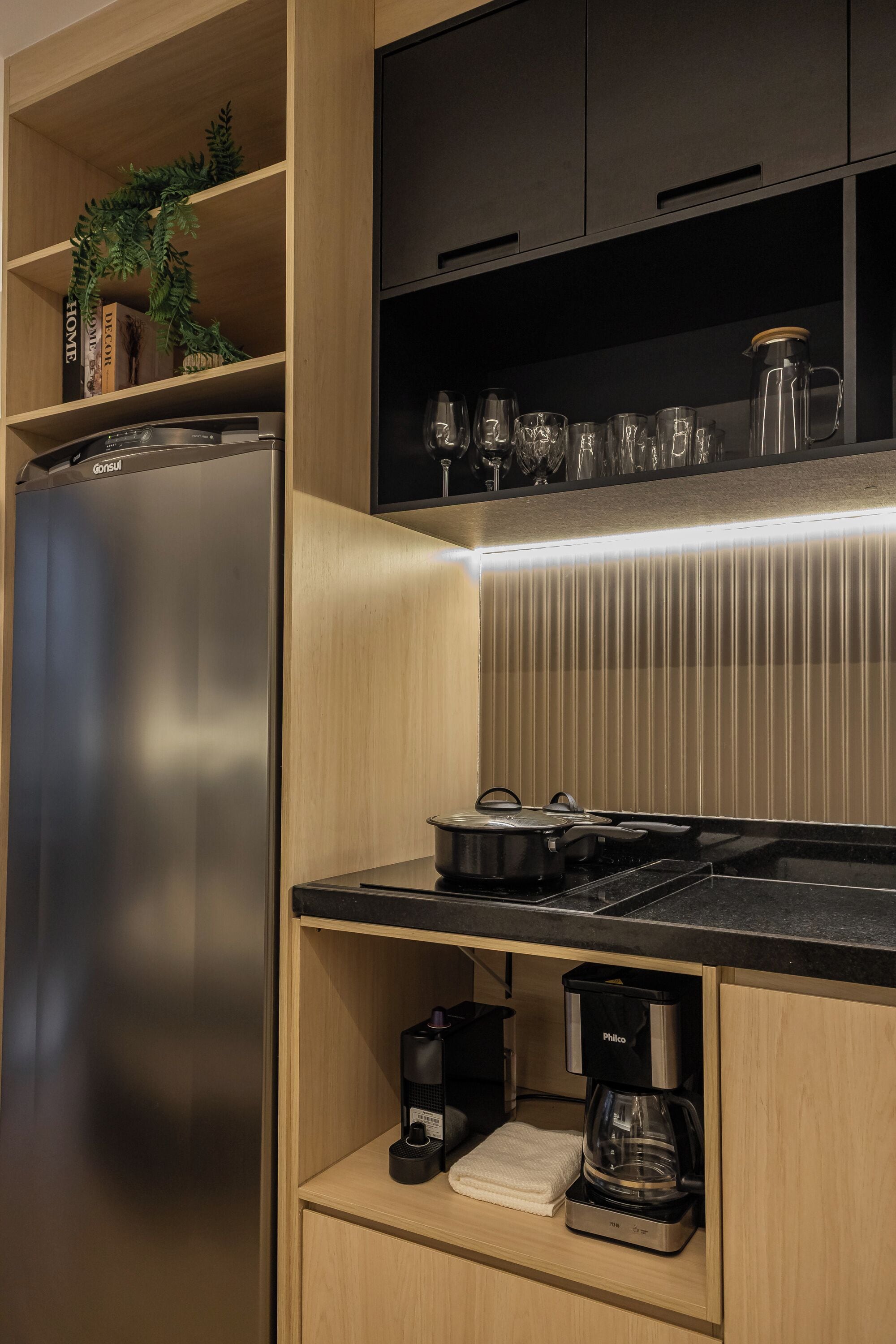 Cocina compacta con refrigerador de acero inoxidable, cafetera y microondas.