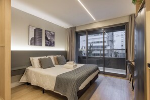 Un dormitorio moderno con una cama grande, un ventanal corredero a un balcón y dos cuadros en la pared.