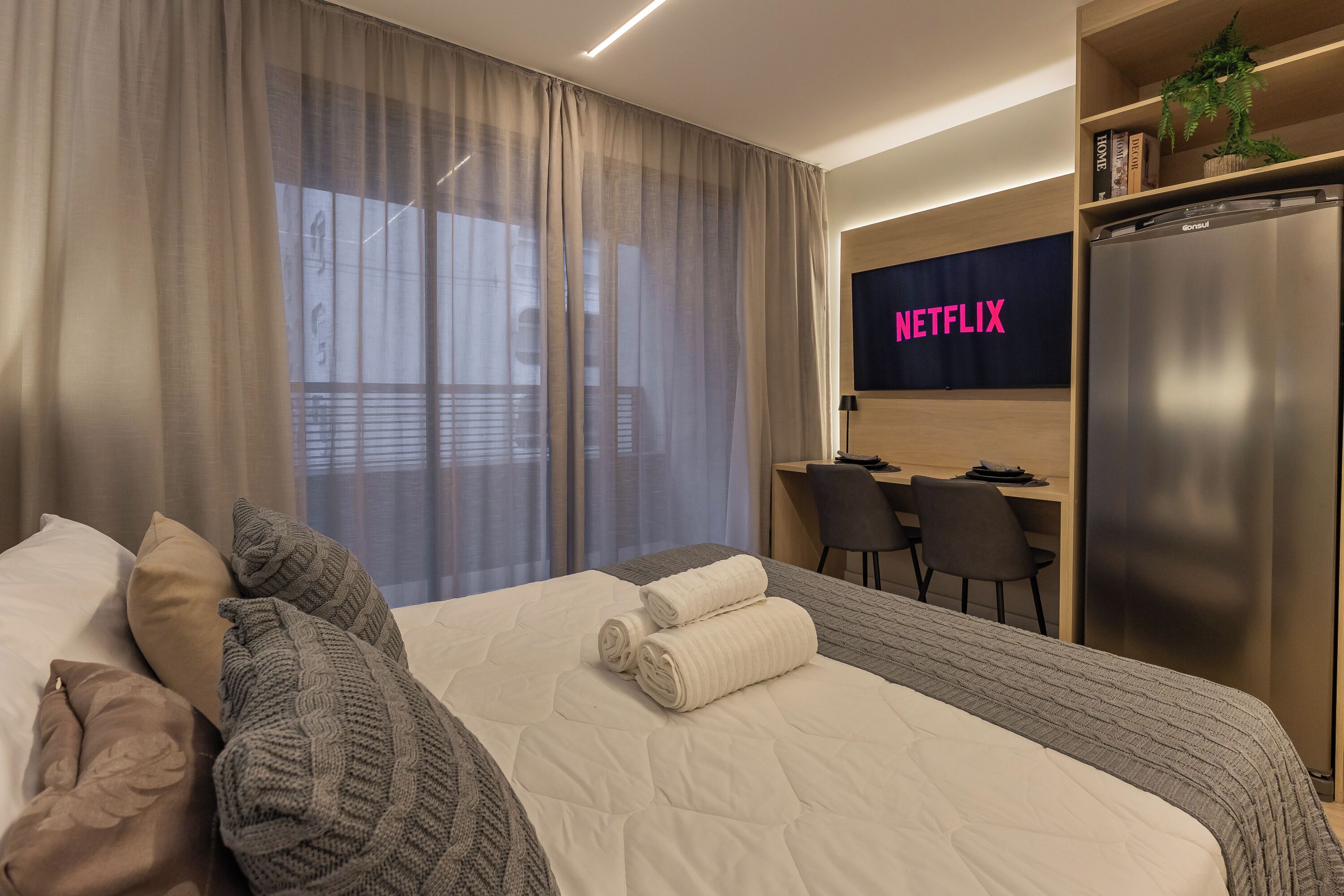 Una camera d'albergo con un letto, una scrivania, una sedia, una televisione e un frigorifero.