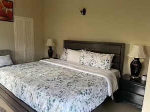 Un dormitorio con una cama, dos mesitas de noche con lámparas, una mesita auxiliar, una lámpara de pared y una puerta con armario.