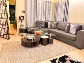 A living room with a sofa, a glass coffee table, and a patterned rug. - Sumfest ~ Draxhall ~ 24hr Gated ~ Pool (St Ann Jamaica)