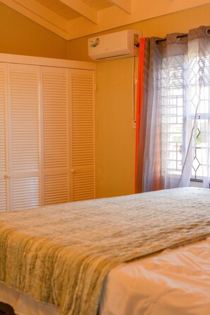 A bedroom with a bed, a window with curtains, and a closed door. - Sumfest ~ Draxhall ~ 24hr Gated ~ Pool (St Ann Jamaica)