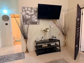 A modern living room with a flat-screen TV mounted on the wall, a black entertainment unit, and decorative vases with branches. - Sumfest ~ Draxhall ~ 24hr Gated ~ Pool (St Ann Jamaica)