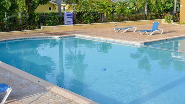A rectangular swimming pool with clear blue water, surrounded by a tiled deck. There are two lounge chairs and a signboard visible in the background. - Sumfest ~ Draxhall ~ 24hr Gated ~ Pool (St Ann Jamaica)