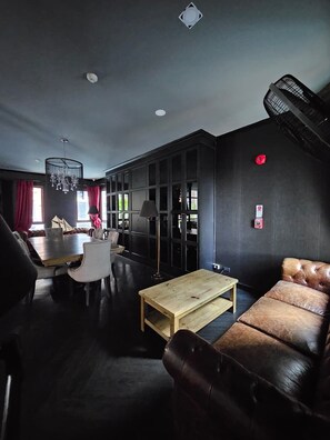 Ein modernes Wohnzimmer mit dunkler Farbgestaltung, einer Ledersofa, einem Holztisch und einem Essbereich mit Tisch und Stühlen.