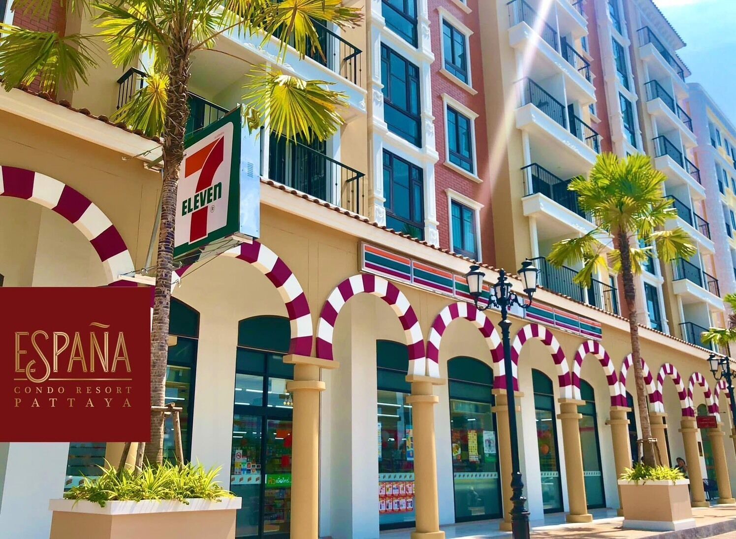 A multi-story building with a prominent 7-Eleven convenience store on the ground floor, a sign for 'ESPANA CONDO RESORT PATTAYA,' and a series of arches with a striped pattern.