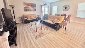 A living room with two sofas, a TV, a ceiling fan, and a dining area with chairs. - Coastal Escape in Sea Grove (Port St. Joe)