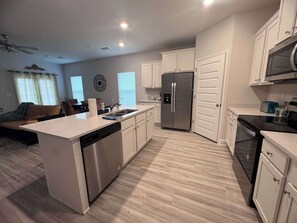 A modern kitchen with a central island, stainless steel appliances, and white cabinetry. - Coastal Escape in Sea Grove (Port St. Joe)