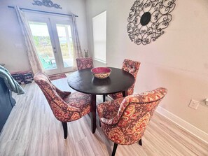 A dining area with a round table, patterned chairs, a decorative wall piece, and a view through a glass door. - Coastal Escape in Sea Grove (Port St. Joe)