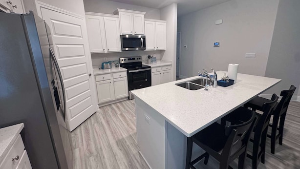 A modern kitchen with white cabinetry, stainless steel appliances, and a central island with seating. - Coastal Escape in Sea Grove (Port St. Joe)