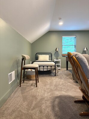A bedroom with a bed, a chair, a lamp, and a window.