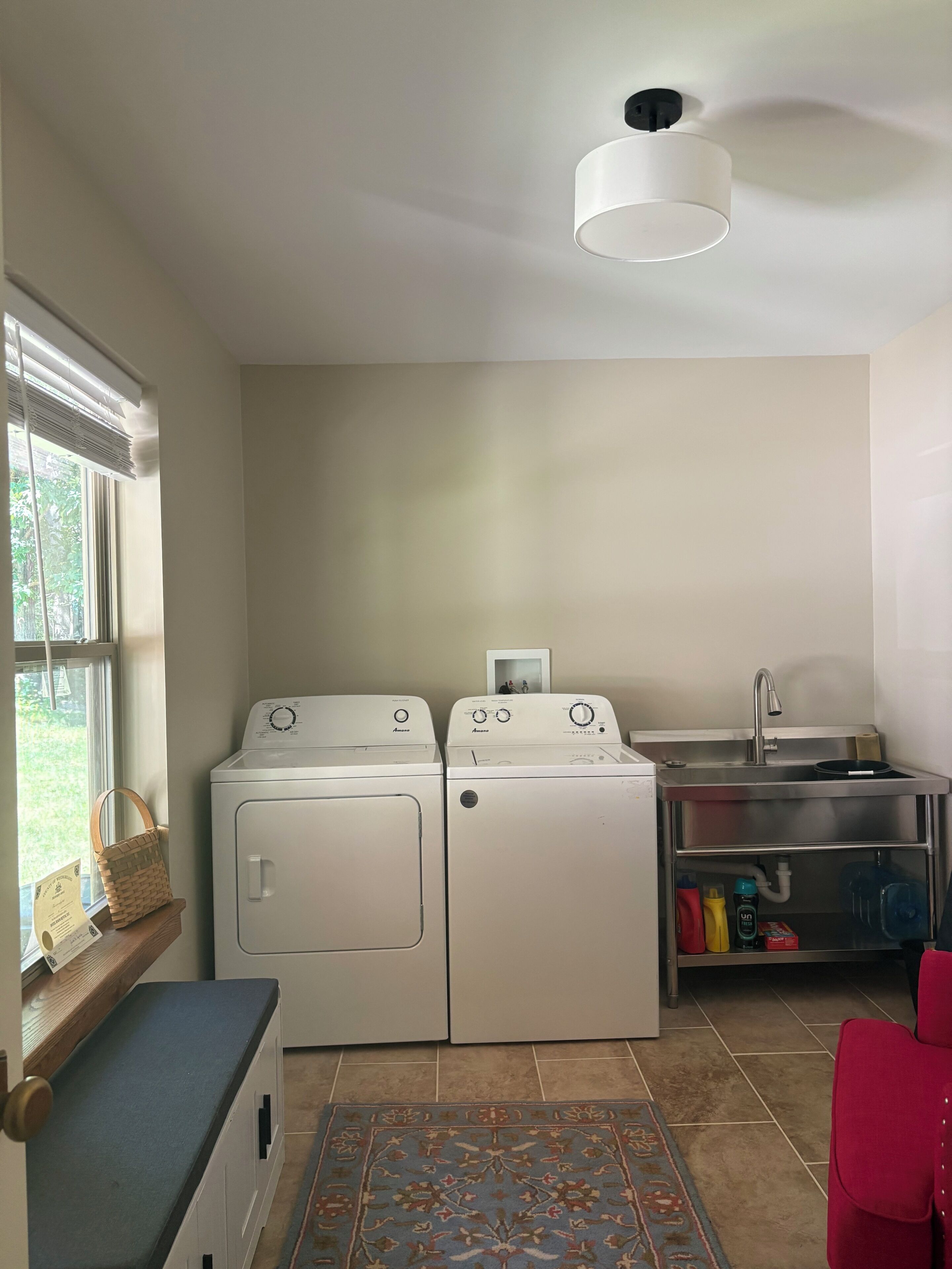 A laundry room with two front-loading washing machines, a sink, and a window with a view of greenery.