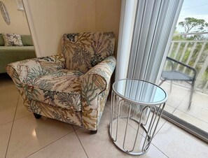 A room with a patterned armchair, a small round table, and a view through a glass door to an outdoor balcony. - Just listed: Bonita Haven – Beach Gear – Near the Gulf (Bonita Springs)