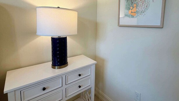 Un comodino bianco con una lampada blu e un'opera d'arte incorniciata a parete.