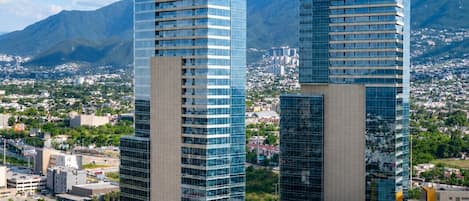 Dos edificios altos con fachadas de vidrio reflectante, rodeados de un paisaje urbano y montañas.