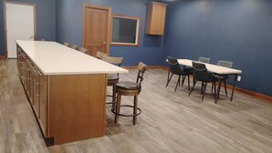 A kitchen with a long island counter, wooden cabinets, and a dining area with a table and chairs. - Black Hills Barking Bunkhouse - Remodeled bldg with all amenities and 3 RV sites (Belle Fourche)