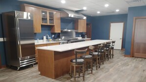 A kitchen with a stainless steel refrigerator, wooden cabinets, a white countertop, and a bar stool seating arrangement. - Black Hills Barking Bunkhouse - Remodeled bldg with all amenities and 3 RV sites (Belle Fourche)