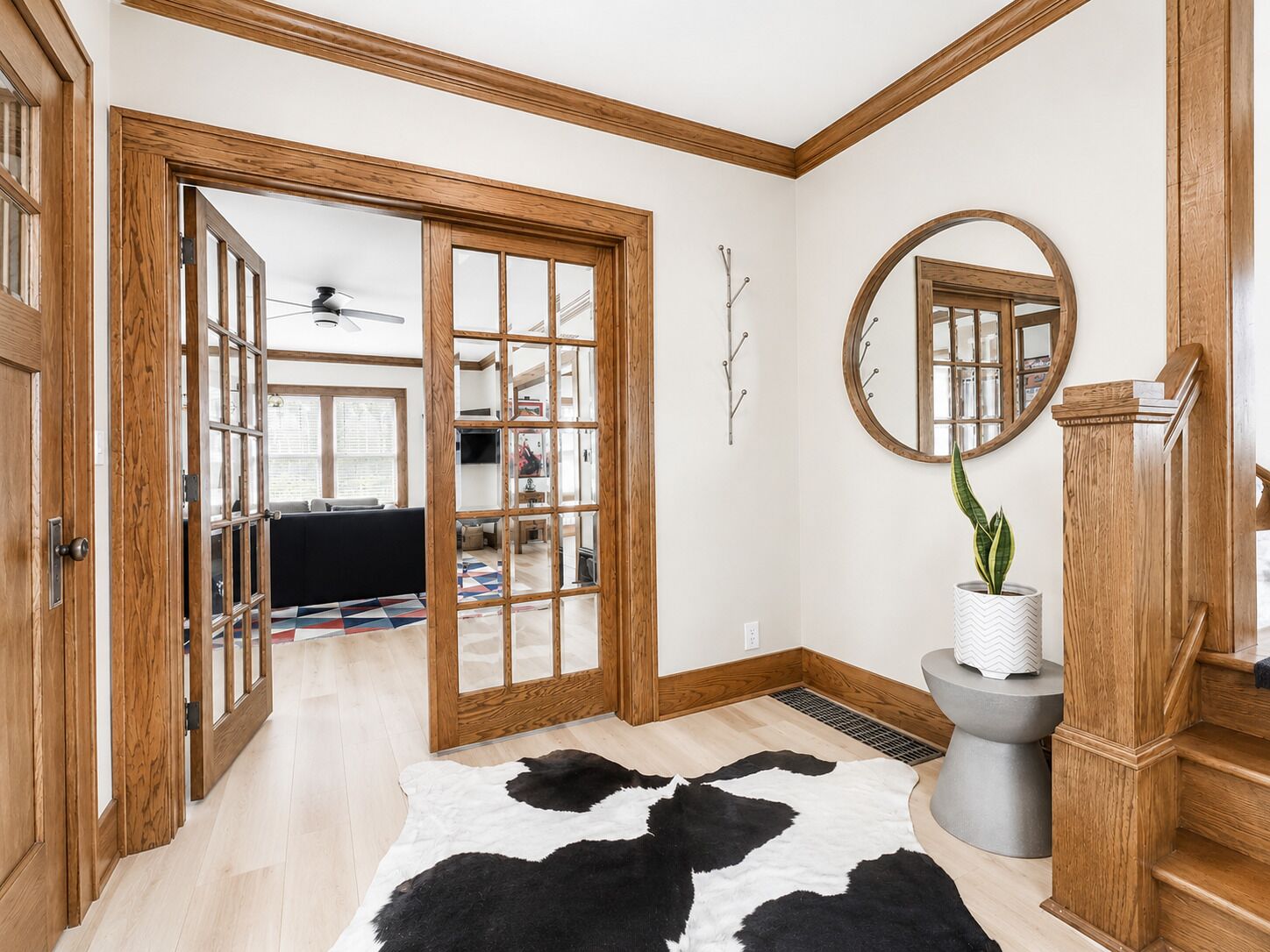 A room with a wooden floor, a cowhide rug, a round mirror, and a staircase with wooden railings.